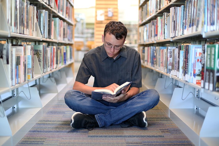 senior boy reading book in isle of library